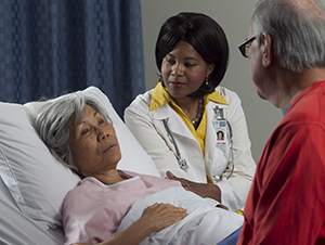 Woman lying in hospital bed with man and health care provider nearby.